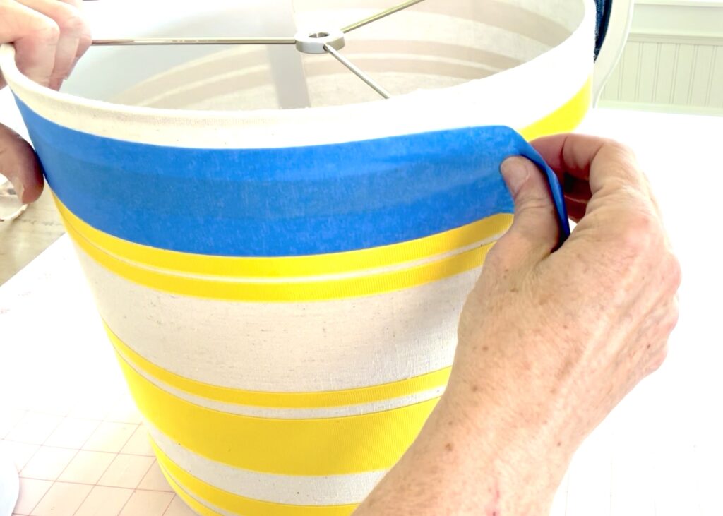 Apply painters tape to create a guide for placing horizonal stripes on a lampsahde. 