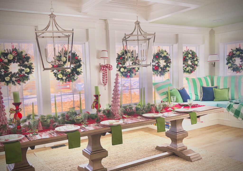 A dining room decorated for Christmas with a very long table, all set for a festive dinner. Wreaths fill the large windows and silver wall sconces and tied with large, buffalo check bows. 