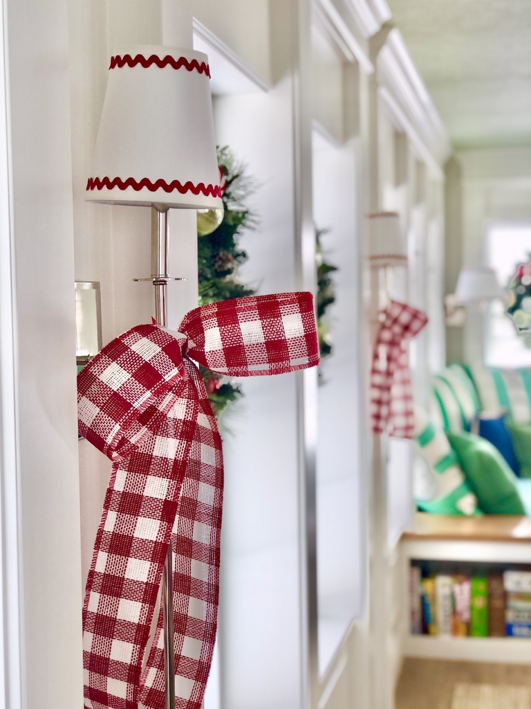 Long silver, polished nickel sconces are topped with festive red rick-rack adorned lamp shades and draped in red & white buffalo checked bows. 