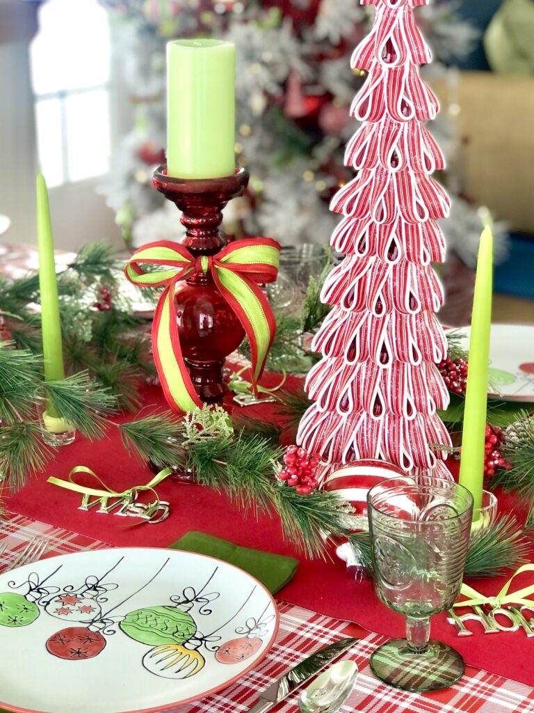 Tall green tapers candles in short class holders accent the greens in the Christmas ornament patterned dinner plates. 