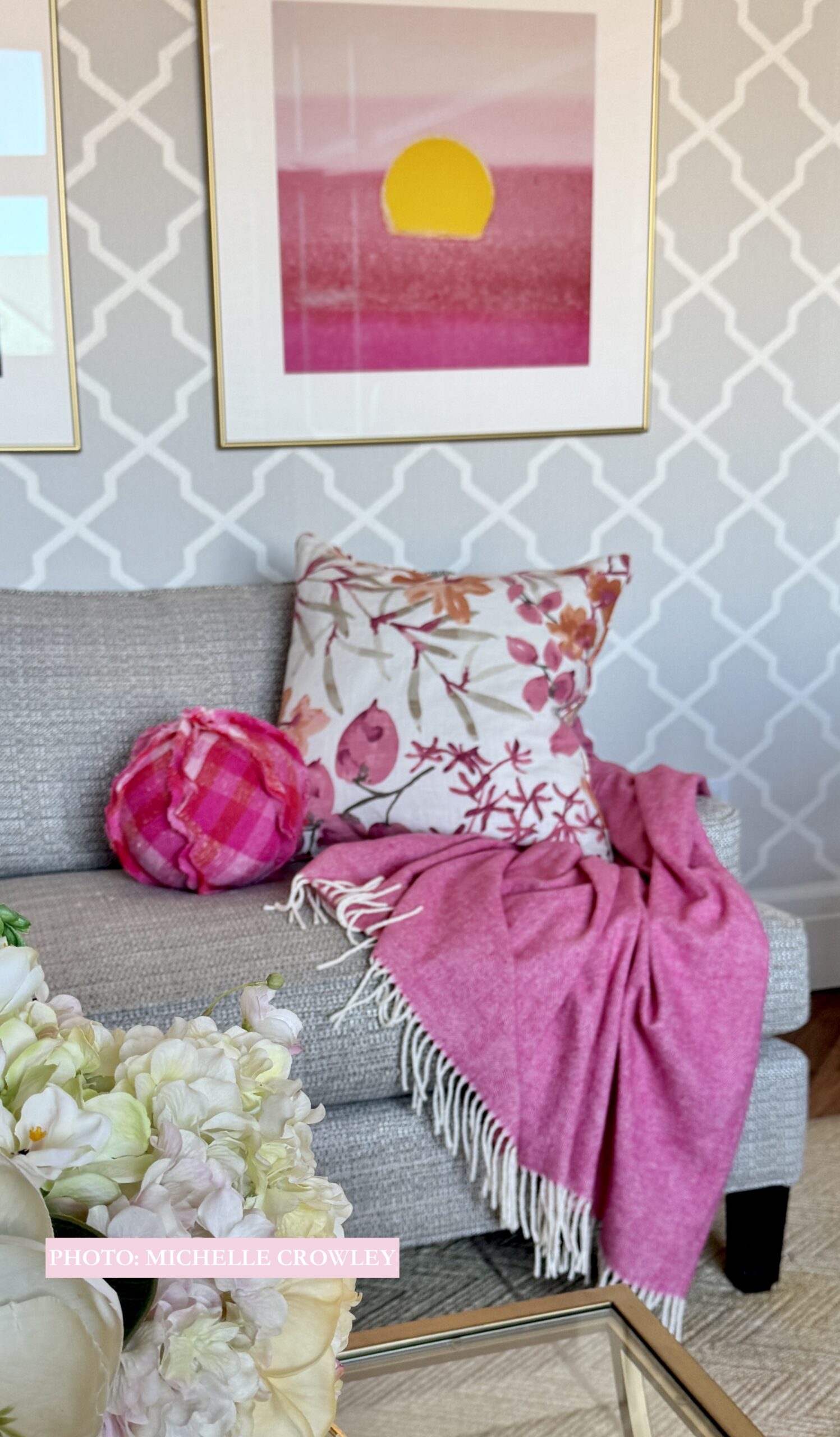 Ball Pillow made in a sweater knit pink & orange buffalo plaid. Sitting on the sofa of a lovely living room with a printed grass cloth wallpaper.